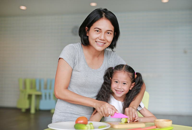 Mamma lär sina barn att laga mat Stäng asiatisk mamma och dotter som skivar gurkgrönsaker på huggtavla i spelrummet arkivbild Mamma lär sina barn att laga mat Stäng asiatisk mamma och dotter som skivar gurkgrönsaker på huggtavla i spelrummet arkivbild