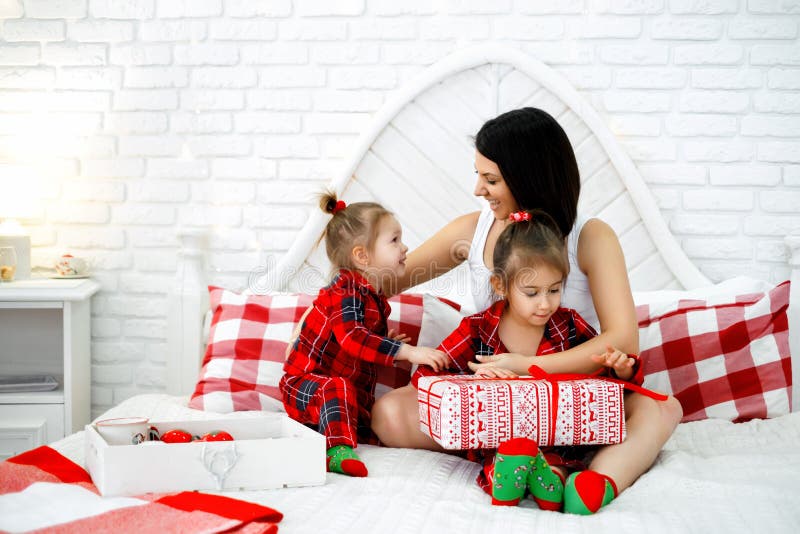 Mamma och barn skrattar medan den äldre flickan öppnar en julklapp arkivfoton