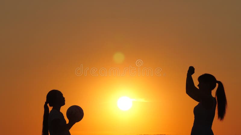 Mamma och dotter leker och kastar boll till varandra under varm sol. glada friska barn som leker med en