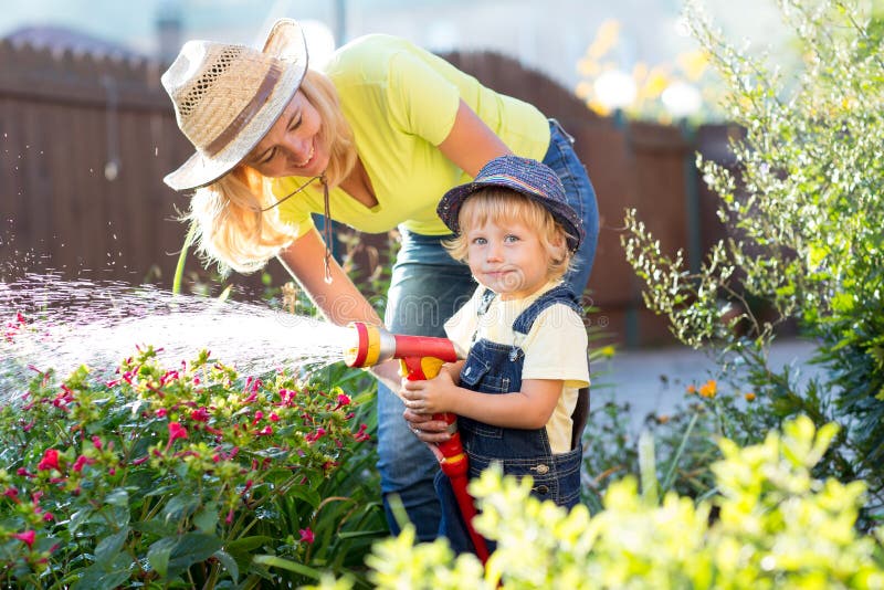 Mamma och liten son som bevattnar blommor i trädgård royaltyfri foto Mamma och liten son som bevattnar blommor i trädgård royaltyfri foto