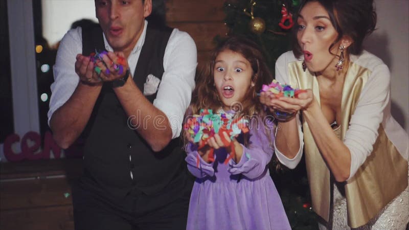 Mamma, papà felice e figlia soffianti celebrazione variopinta dei coriandoli del Natale