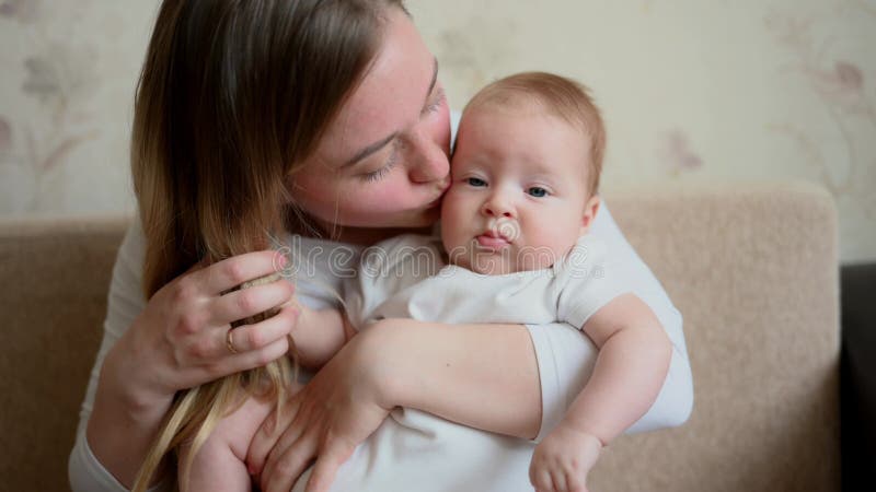 Mamma tiene abbracci bacia il suo bambino mostrando il suo amore seduto sul divano di casa. tocco di amore tra madre e bambino video d archivio