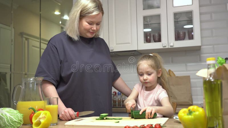 Mamma visar sin dotter hur man skär grönsaker för en hälsosam middag arkivfilmer