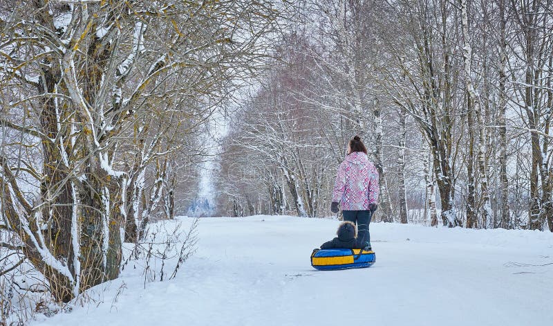 Mamman rullar hennes lilla son på rör i parkerar i vintern lycklig familj utomhus vintergyckel för unga barn royaltyfri fotografi Mamman rullar hennes lilla son på rör i parkerar i vintern lycklig familj utomhus vintergyckel för unga barn royaltyfri fotografi