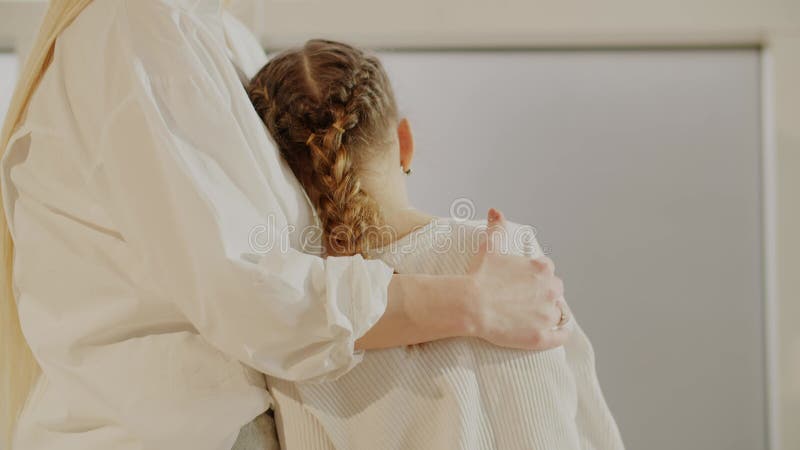 Mamá abraza suavemente a su hija y se acaricia el hombro. mamá y su hija vestidas de blanco. el concepto de felicidad metrajes