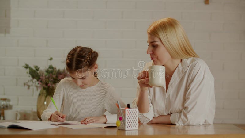 Mamá bebe su café y controla cómo su hija preadolescente hace su tarea. el concepto de ayuda y elogio de almacen de metraje de vídeo