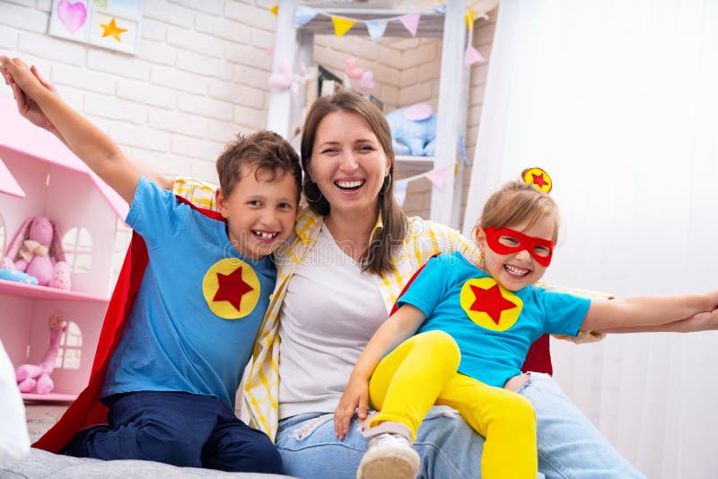Mamá e hija hermosas de la familia con el hijo vestido en trajes de superhéroes en máscaras y la diversión roja de las capas para fotografía de archivo libre de regalías Mamá e hija hermosas de la familia con el hijo vestido en trajes de superhéroes en máscaras y la diversión roja de las capas para fotografía de archivo libre de regalías
