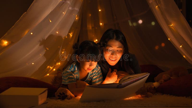 Mamá leyendo un cuento de hadas para su hija en una tienda de niños antes de irse a la cama foto de archivo
