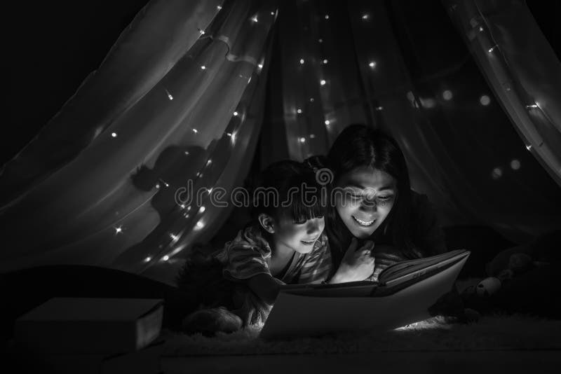 Mamá leyendo un cuento de hadas para su hija en una tienda de niños antes de irse a la cama fotos de archivo