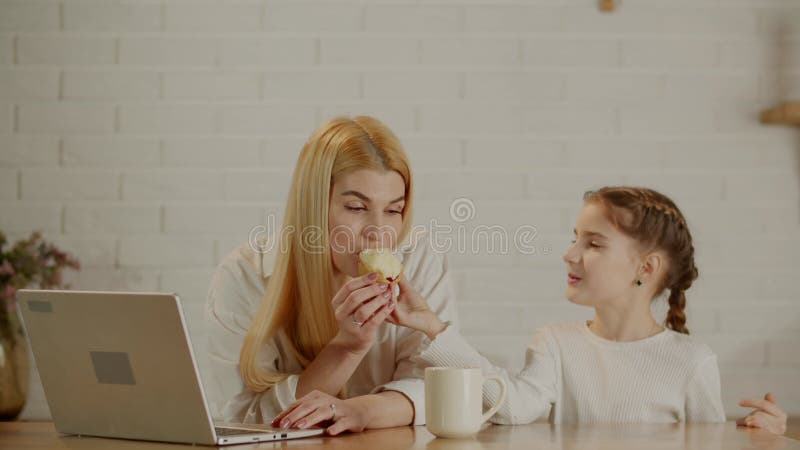 Mamá trabaja en una laptop y su hija la trata a un bizcocho. asistente de madres. almacen de metraje de vídeo
