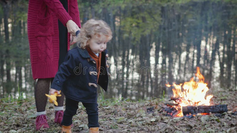 Mamã e caminhada pequena do filho em torno da fogueira perto do lago do outono