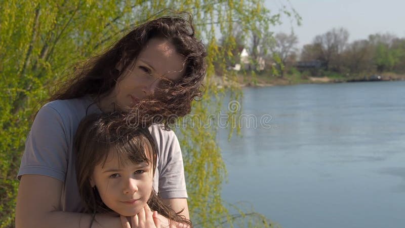 Mamã e filha no banco de rio Mulher com criança em um dia ensolarado pela água Família feliz na natureza