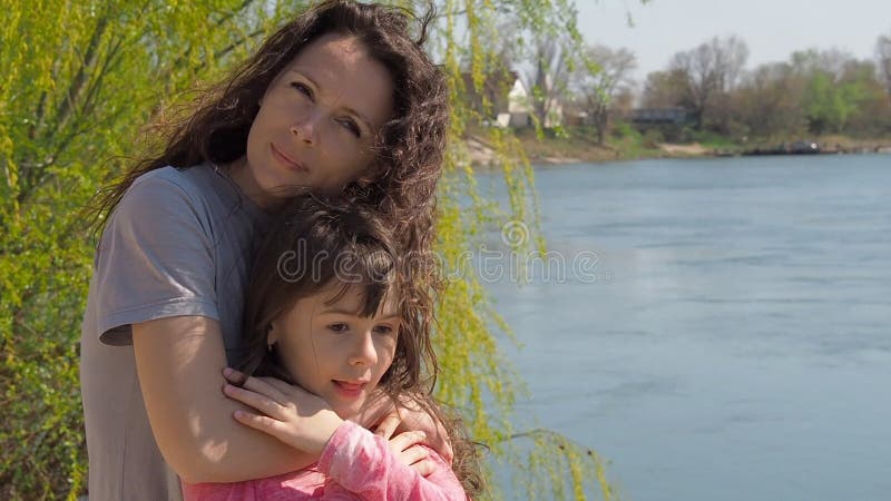 A mamã está abraçando sua filha pelo rio Uma menina com sua mãe pela água Família no ar livre