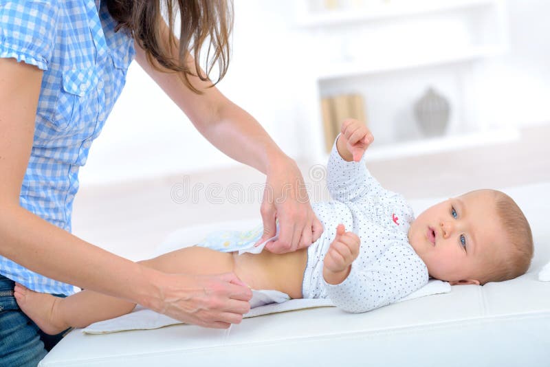 A mamã põe sobre a tabela em mudança do bebê do tecido fotografia de stock A mamã põe sobre a tabela em mudança do bebê do tecido fotografia de stock