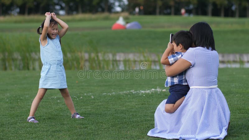 Mamã que fotografa a menina asiática engraçada no parque