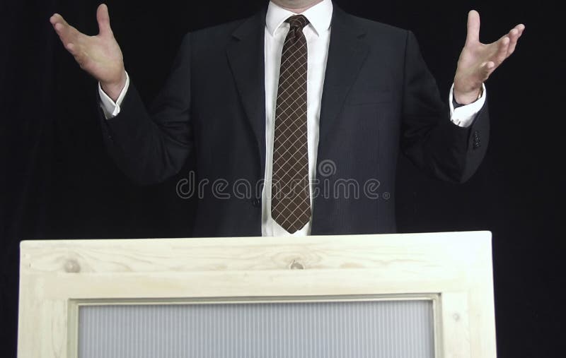 Man addressing crowd on podium with expressive hands