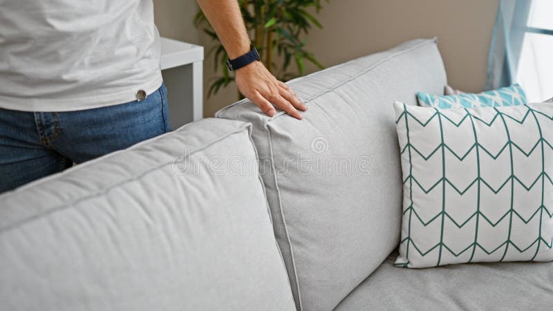 Man adjusting cushion on a modern sofa in a cozy home interior with decorative pillows stock image