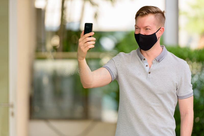 Man använder ansiktsmask för att skydda mot coronavirus covid19 när man använder mobiltelefon royaltyfria foton