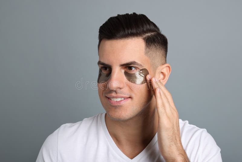 Man Applying Dark Under Eye Patch on Grey Background Stock Image