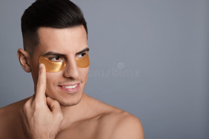 Man applying golden under eye patch on grey background. Space for text royalty free stock photo