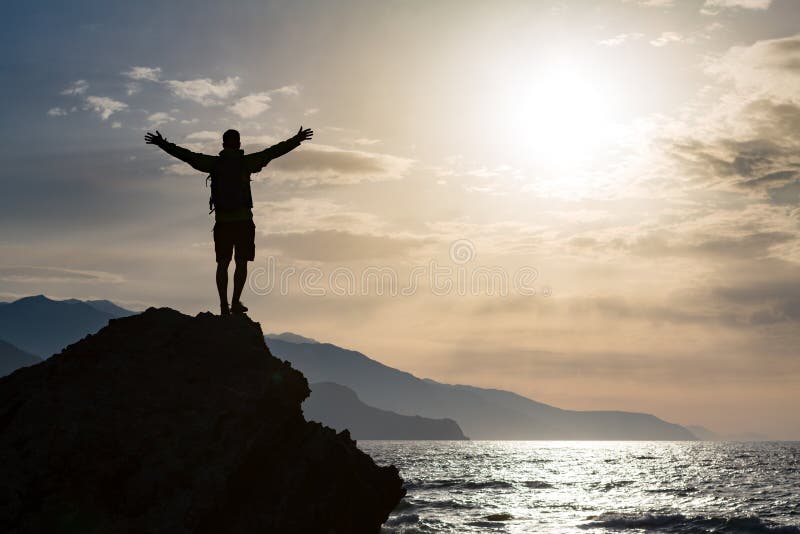 Man with arms outstretched celebrating or praying in beautiful inspiring sunrise with mountains and sea. Man hiking or climbing with hands up enjoy inspirational landscape on rocky top on Crete. Man with arms outstretched celebrating or praying in beautiful inspiring sunrise with mountains and sea. Man hiking or climbing with hands up enjoy inspirational landscape on rocky top on Crete.