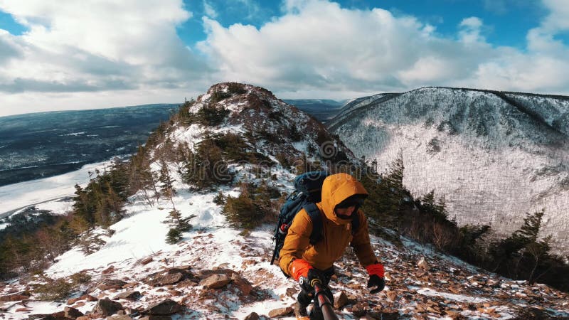 Man ascending snowy mountain along the Cabot Trail in Nova Scotia, Canada. The ocean behind him stock video footage