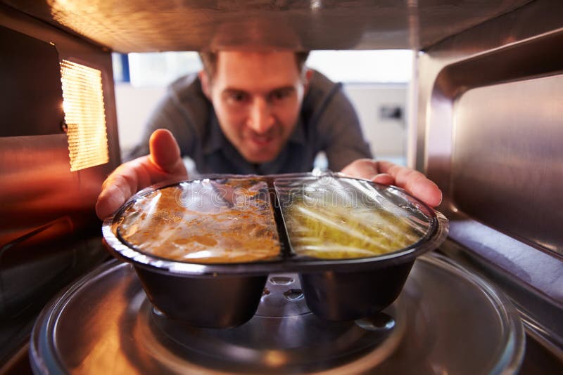 Man Putting TV Dinner Into Microwave Oven To Cook. Man Putting TV Dinner Into Microwave Oven To Cook