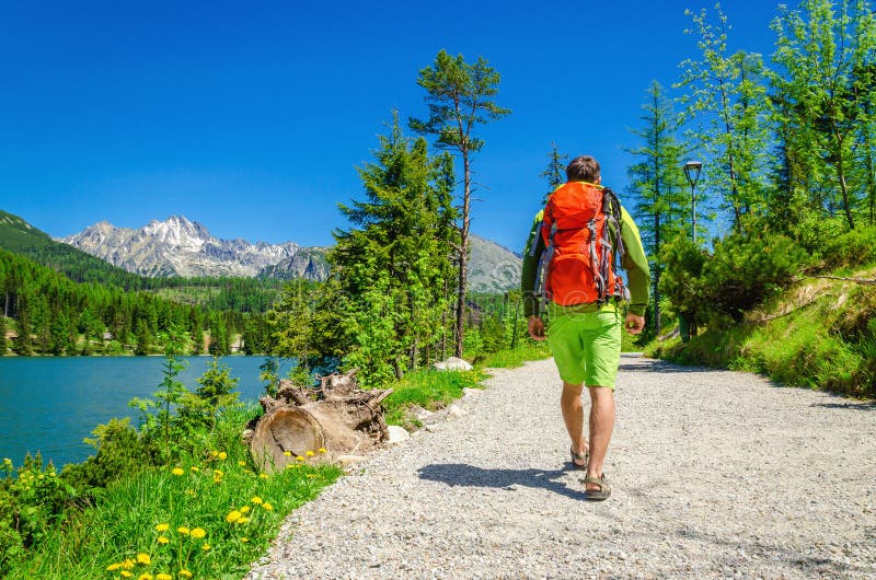 Man with backpack walks mountain trail by lake