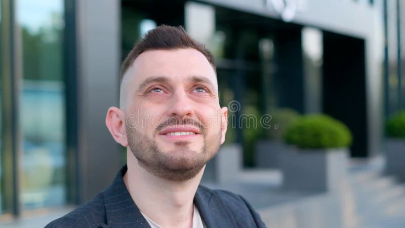 A man with a beard on his face smiles contentedly in front of the building. Close up