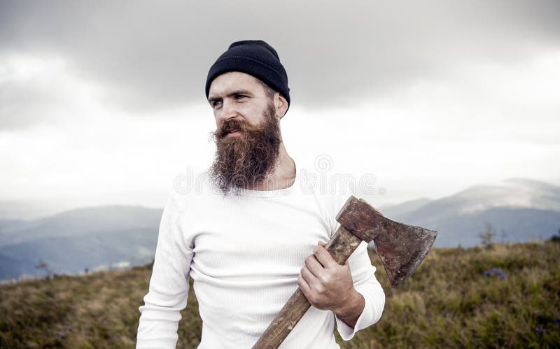 Man with beard holds axe on mountain with cloudy sky