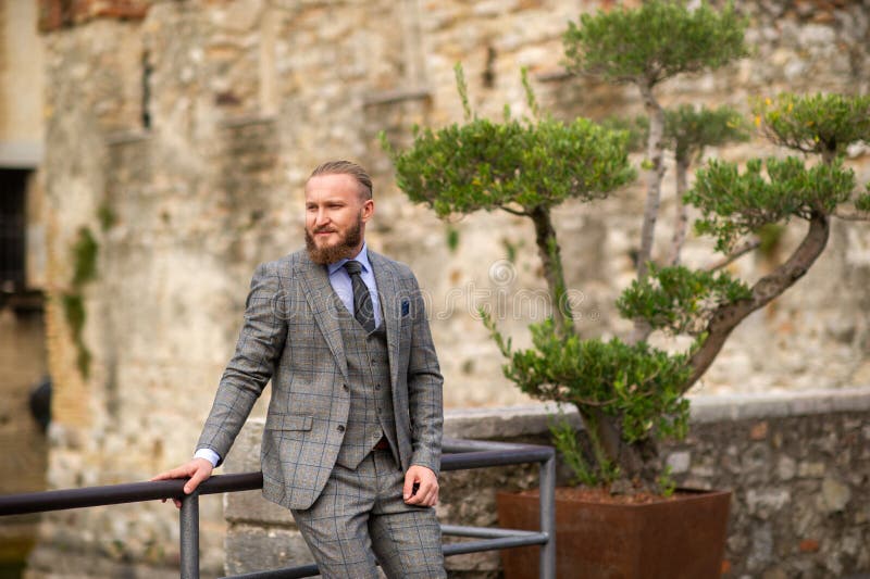 A man with a beard in a strict grey three-piece suit with a tie in the old town of Sirmione, a Stylish man in a grey suit in Italy