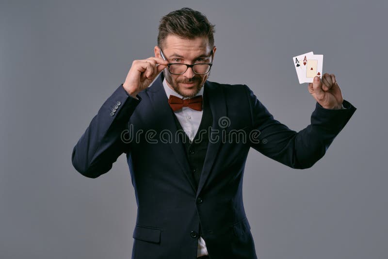 Man in black classic suit, red bow-tie, glases is showing two playing cards, posing on gray studio background. Gambling royalty free stock photos