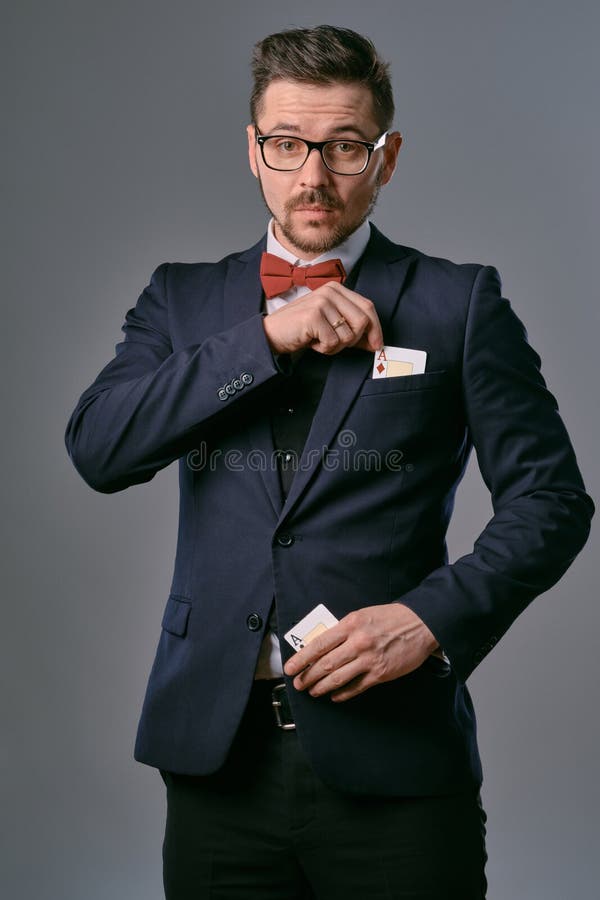Man in black classic suit, red bow-tie, glases is showing two playing cards, posing on gray studio background. Gambling stock photography