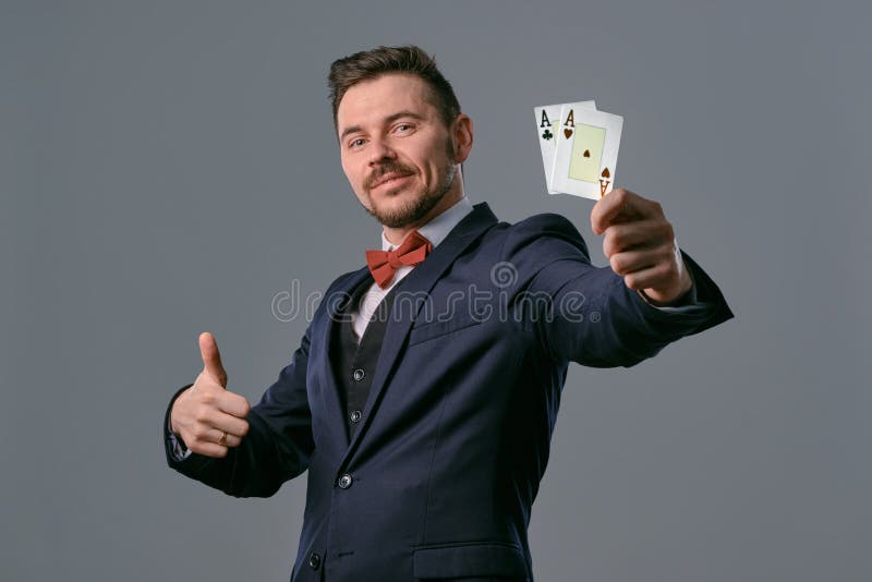 Man in black classic suit and red bow-tie showing two playing cards while posing against gray studio background royalty free stock photo