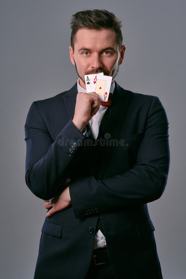 Man in black classic suit and red bow-tie showing two playing cards while posing against gray studio background stock image