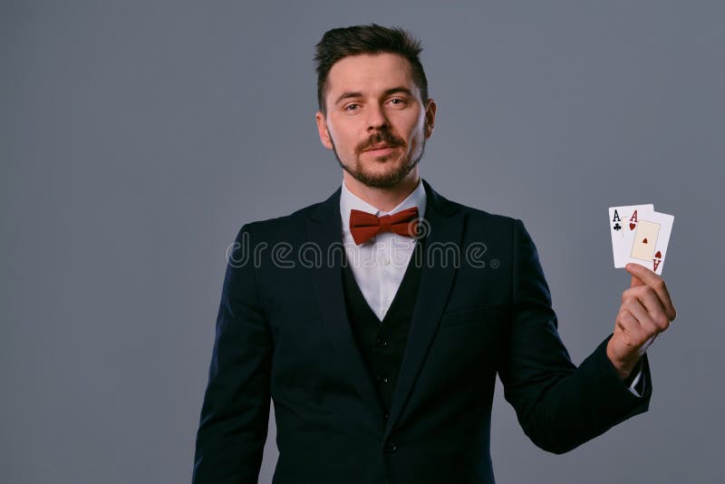Man in black classic suit and red bow-tie showing two playing cards while posing against gray studio background royalty free stock photo