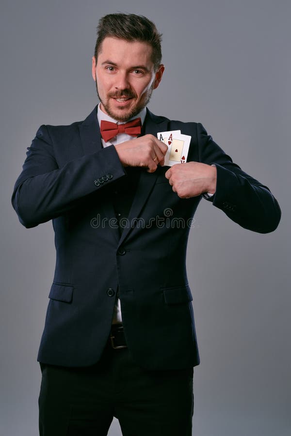 Man in black classic suit and red bow-tie showing two playing cards while posing against gray studio background royalty free stock photography