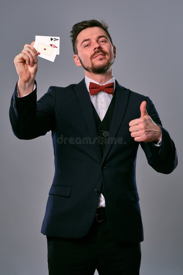 Man in black classic suit and red bow-tie showing two playing cards while posing against gray studio background stock photography