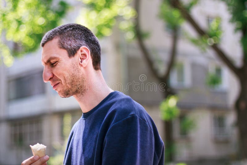 Man in blue pulover eating icecream in the park stock photos Man in blue pulover eating icecream in the park stock photos