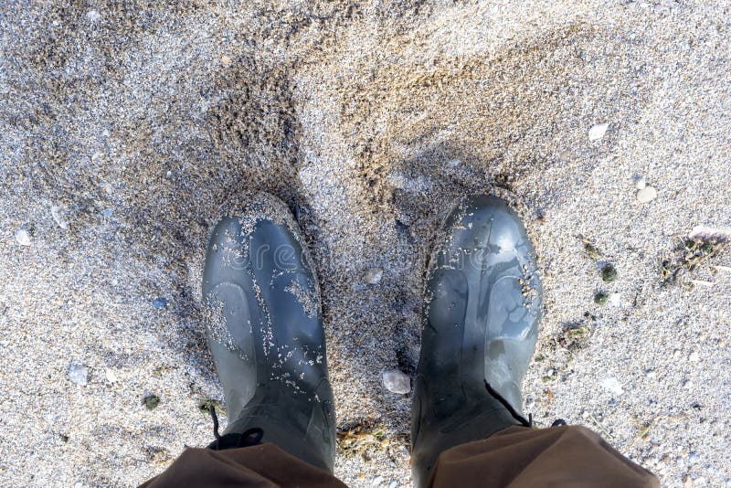 Man in Brown Pants and Rubber Boots on the Sandy Beach Stock Photo