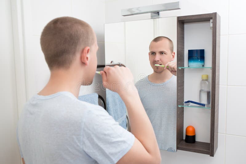 Man Brushing Teeth and Looking at Mirror in Bathroom Stock Image