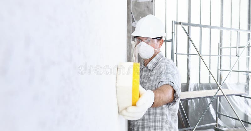 Man builder using a sponge on  wall professional construction worker with mask, safety hard hat, gloves and protective glasses.