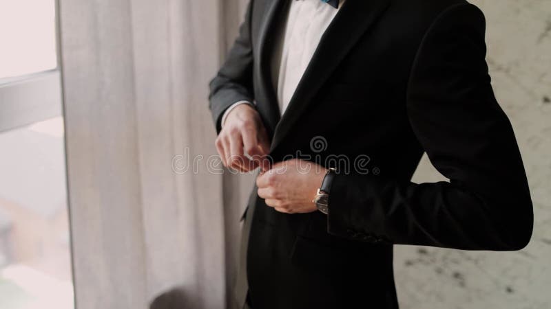 A man buttons a button of a black jacket