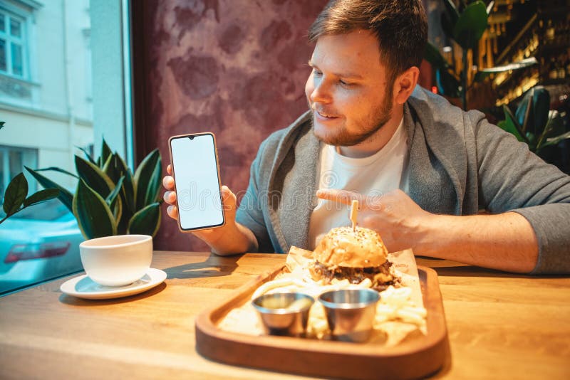 Man in Cafe Holding Phone with White Screen Eating Burger Stock Photo ...
