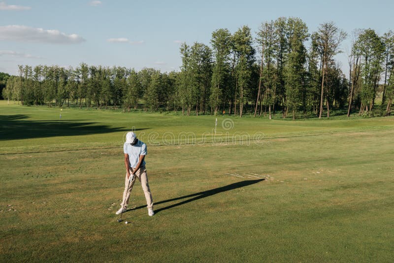 Man in cap holding golf club and hitting ball on green lawn