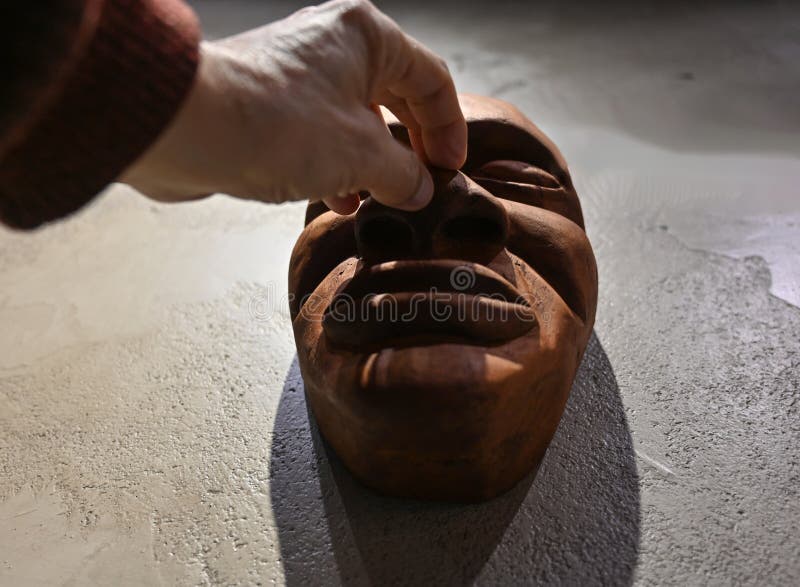 Man carefully pressing on the nose of a wooden mask resting on a textured surface stock images