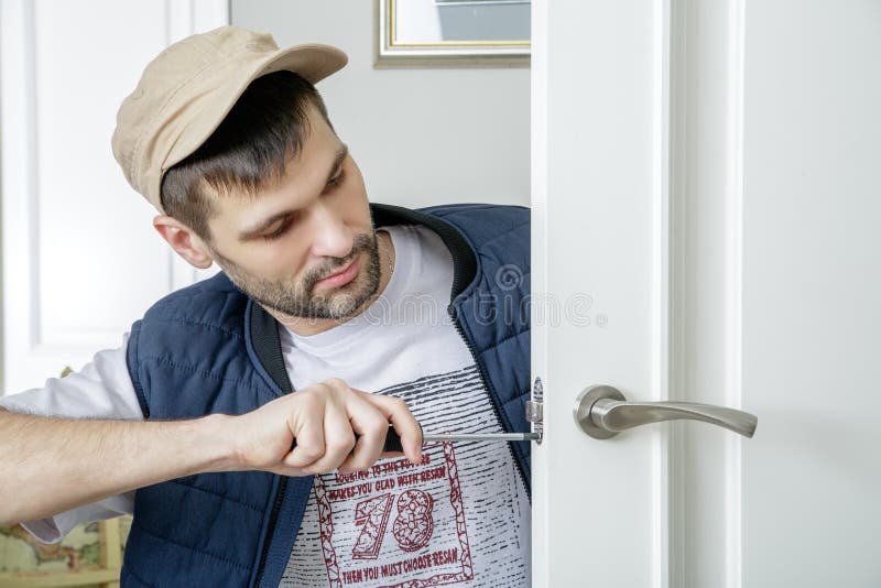Man carpenter fixing lock in door with screwdriver at home. stock photo Man carpenter fixing lock in door with screwdriver at home. stock photo