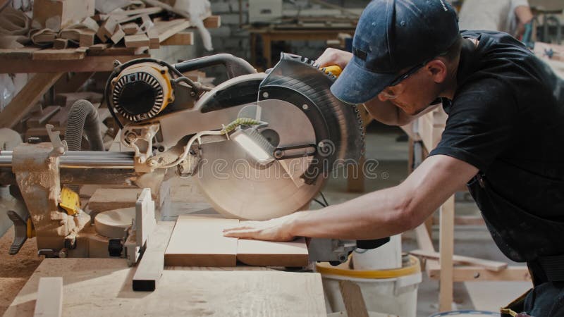 Man in a carpentry workshop cutting a small pieces of the wooden detail using a big circular saw