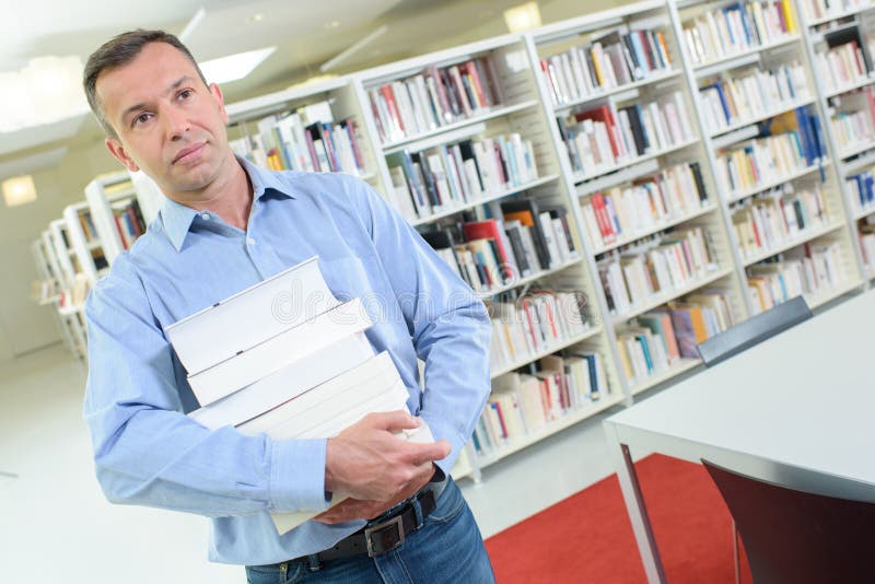 Man carrying stack books in library stock photo