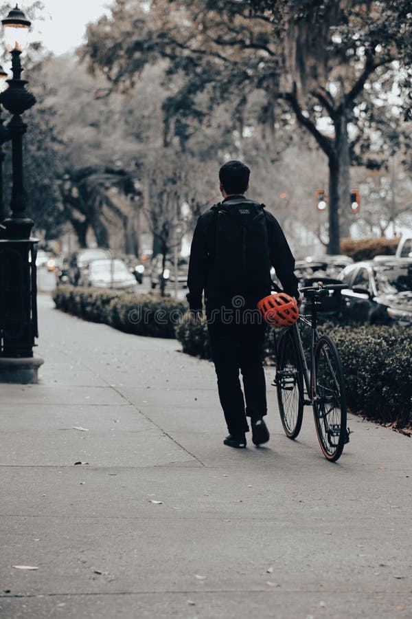 Man in Casual Attire Walking Down an Urban Sidewalk Carrying a Bicycle ...